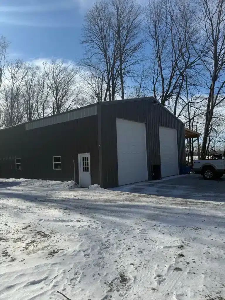 Dark charcoal steel workshop with white roll-up door in snow