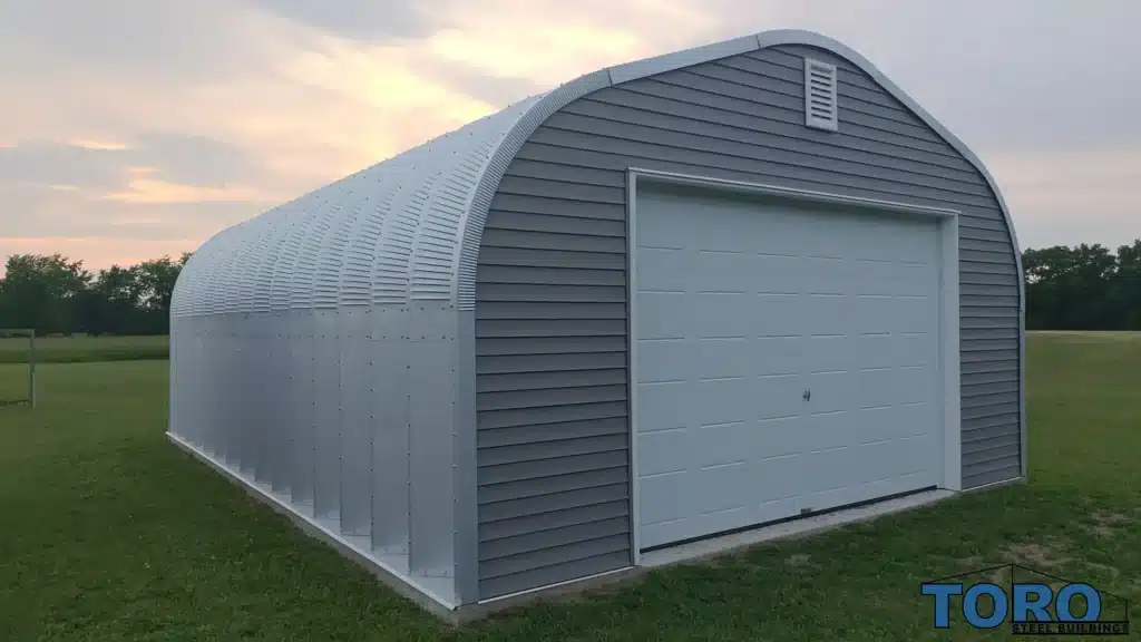 Grey arch-style steel Quonset hut with roll-up door.